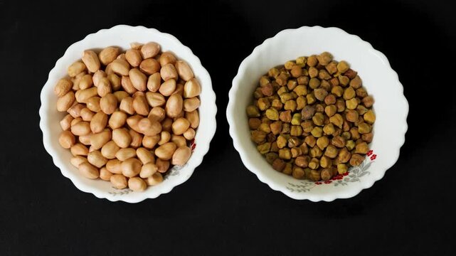 raw peanuts and black chickpeas in ceramic bowls isolated on black background
