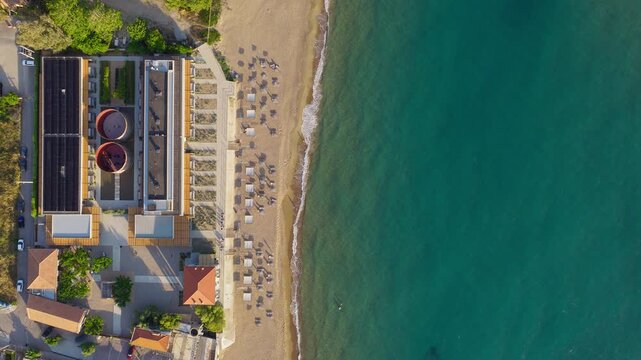 Top down drone shot of Kourouta beach, Greece. Dexamenes Seaside Hotel umbrellas, bathers and swimmers visible. Clear summer day. Aerial beach stock footage