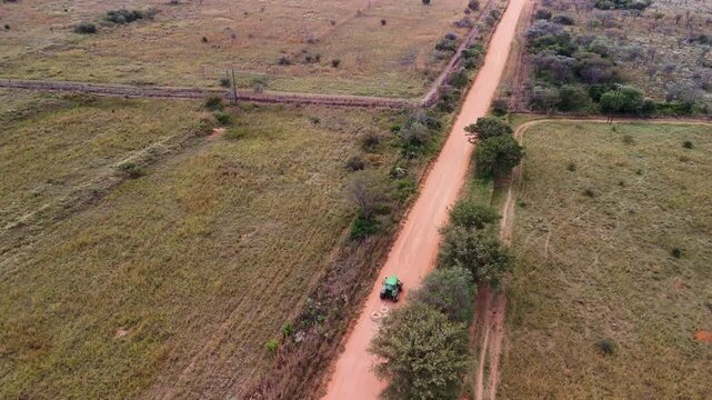 Drone footage, tractor pulling old tyres along a rural dirt road to maintain it