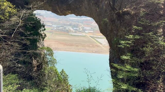 Scenic view through the Danyang Stone Gate, featuring rocky cliffs, forest vegetation, and tranquil waters