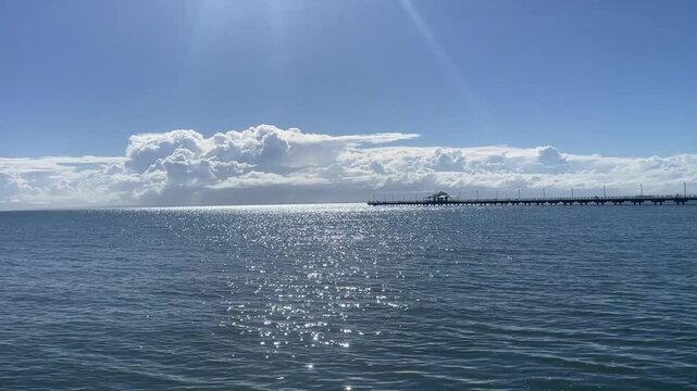 Clear blue water on a sunny day with Sandgate Pier visible in the distance, showcasing a peaceful coastal scene along the Queensland shoreline in Australia.