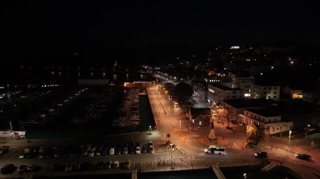 St Peter Port Guernsey at night.Forward drone footage over Albert Pier and Marina along South Esplanade with lights reflecting in calm water with vibrant night time townscape and passing traffic