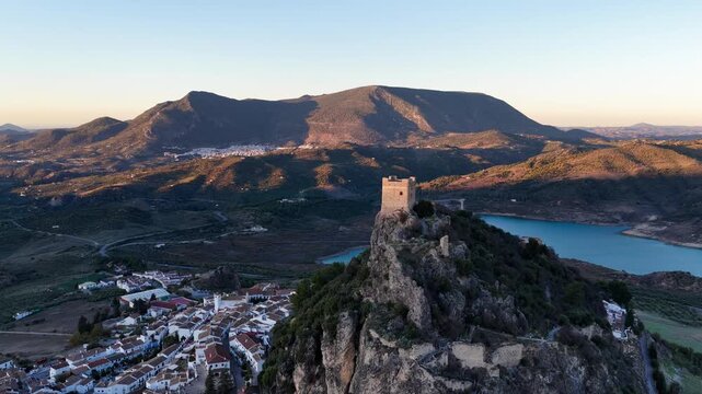 Aerial view of Zahara de la Sierra Castle on a rocky crag overlooking the white village and turquoise reservoir at sunset in Zahara de la Sierra, Andalucia, Spain.