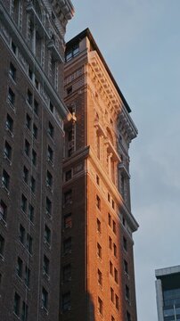 Golden hour sunbeam moving across brick facade of vintage residential building in downtown New York, illuminating ornate architectural details and cornices