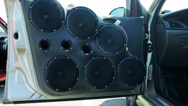 Detailed view of custom car door interior panel featuring elaborate audio setup. Several large subwoofers, mid-range speakers, and small tweeters are integrated. High-quality sound system for vehicle 