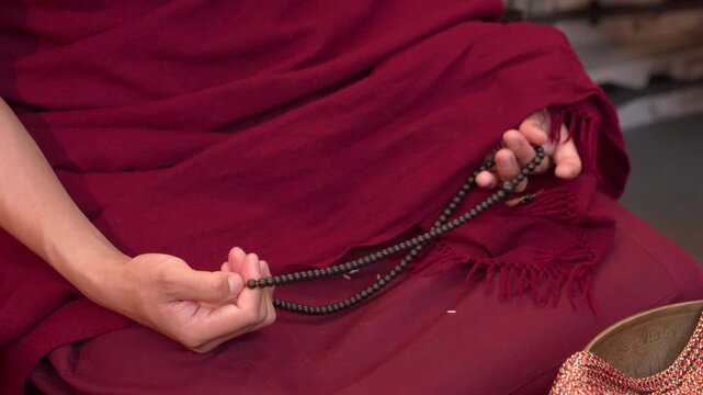 Close-up of the hands of a Tibetan Buddhist monk wearing his red robe and holding a prayer beads.