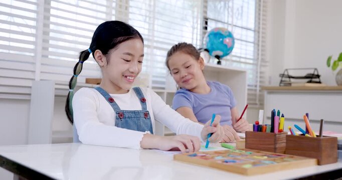 Asian girl in denim overall drawing picture with pencil while caucasian classmate looking, students engaged in childhood creativity and learning, teamwork and cooperation in classroom school education