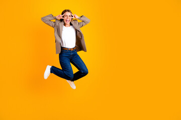 Obraz premium Young woman jumping joyfully on a yellow background in jeans and blazer celebrating fun and energy