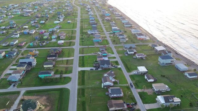 Coastal grid frontage spans Seashell Dr neighborhood stretching toward beachfront corridor, Bluewater Highway forming inland edge. Mixed roof hues, warm lawn color elevated home in Freeport, TX