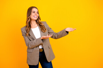 Smiling business woman presenting with open palms on a bright yellow background, confident...