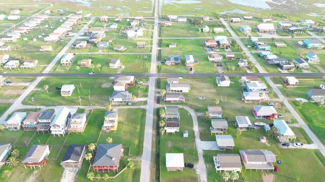 Marshside residential grid captures stilted homes arranged along intersecting Surfside Beach streets bordered by wetlands stretching toward inland water channels. Clean yards in Freeport, Texas