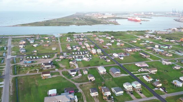 Residential rows west of Seashell Dr extend toward marsh edge facing industrial port across channel. Varied roof colors, trimmed lawns emphasize stilted structures elevated in Freeport, Texas