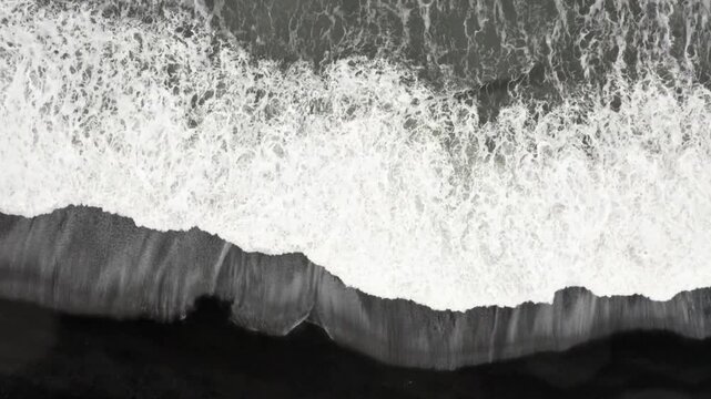 Aerial view of white ocean foam crashing on black sand beach