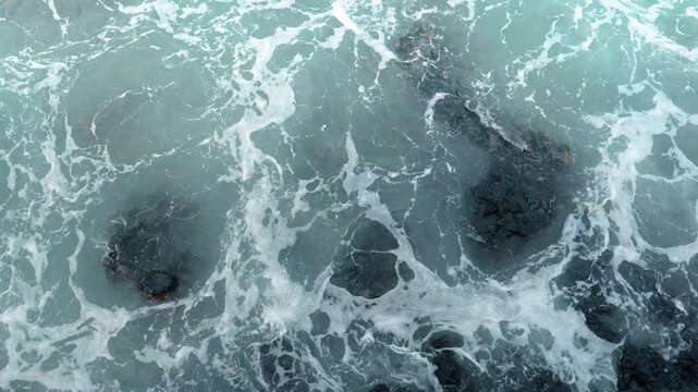 Overhead view of swirling ocean waves, Isabela Island, Galapagos. Top down perspective of white sea foam washing over dark volcanic rocks in turquoise water.