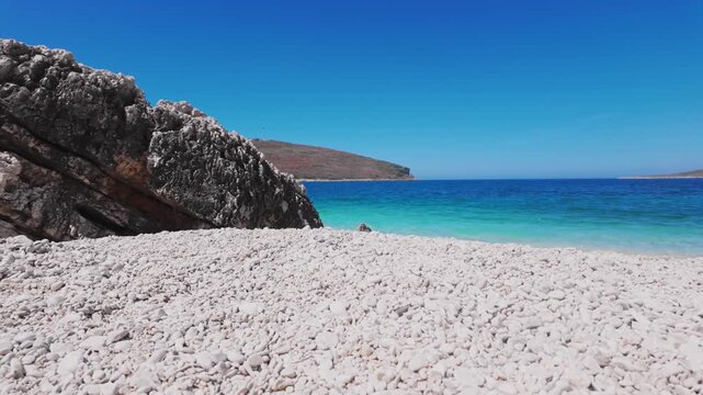 White Pebble Beach With Massive Rocky Cliff And Turquoise Ocean Background, Himare - Albania.