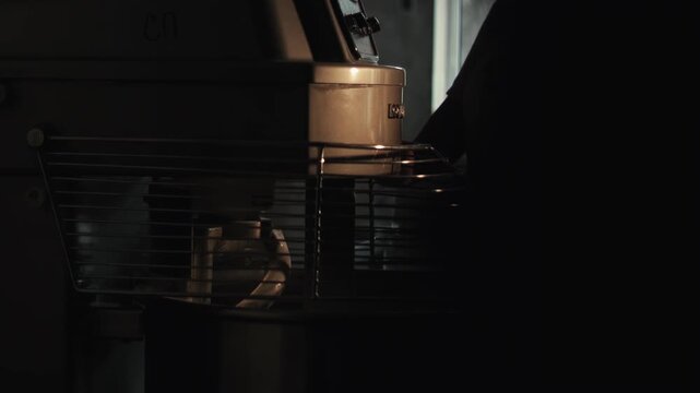 Baker lowers protective metal grate into place over large stainless steel bowl of industrial spiral dough mixer. Hand presses control panel buttons activating electromechanical machine to begin dough 