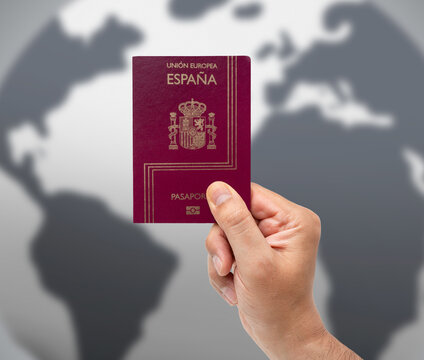 Close-up of hand of man holding Spanish passport over map background.