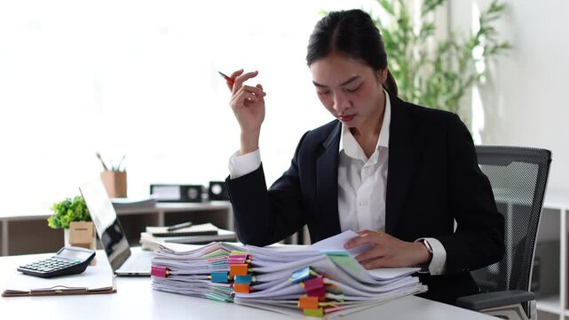 Frustrated businesswoman searching for documents in a large stack of paperwork, feeling stressed and overwhelmed by her workload and approaching deadlines in a busy office
