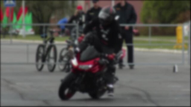 Motorcycle stunt rider in full protective gear balancing on seat of sport motorcycle. Performance takes place at outdoor event, with spectators and barriers. Dynamic display of motorcycle control and 