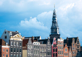 Naklejka premium A striking view of Amsterdam's Westertoren above historic canal houses, beautifully illuminated by the cool spring morning