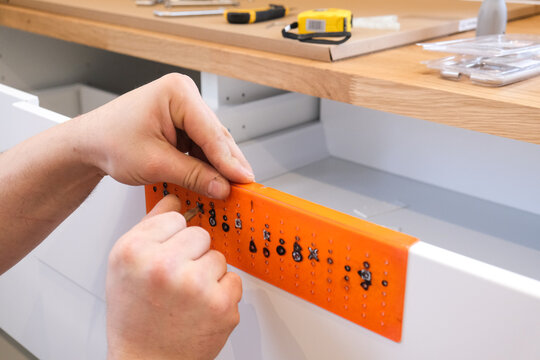 Person attaching drawer slide jig to white kitchen cabinet drawer