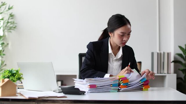 Stressed asian businesswoman overwhelmed with paperwork, having a headache from overworking and feeling tired from managing a large pile of documents in a busy office