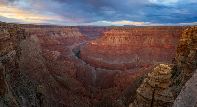 View of the Grand Canyon featuring layered red rock formations under a dramatic cloudy sky at sunset Coconino County, Arizona, United States.
