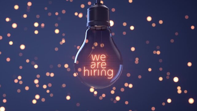 "We are hiring" written on the illuminated filament of a light bulb with a blurred blue background.