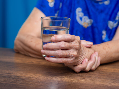 Senior woman with hand tremor holding glass of water