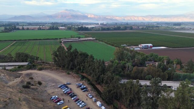 Vehicles parked at the foot of the hill with hectares of green plantations in the background, El Monte commune, Metropolitan Region, country of Chile