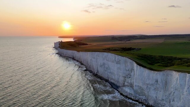 Smooth drone flight along the dramatic white chalk cliffs of Beachy Head during sunset, with golden reflections across the English Channel in East Sussex, England.