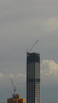 Timelapse video showing a high-rise building under construction with cranes, while clouds move across the sky in the background.