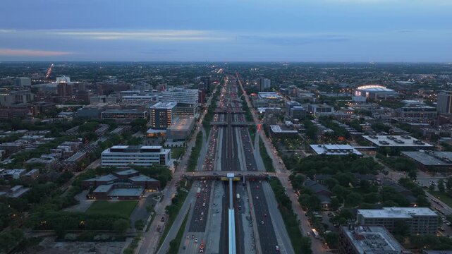 Eisenhower Expressway traffic showing cars with lights on and UIC Campus buildings during blue hour in Chicago, Illinois with United Center stadium background