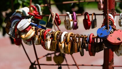 A close-up of numerous colorful and rusty love padlocks locked onto a metal fence as a symbol of...
