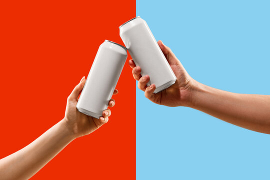 Blank aluminum cans held by two hands in a toast gesture over split red and blue background. Concept of drink brand promo, packaging design, party invite and beverage ad layout.
