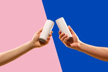 Two blank aluminum cans held in a toast gesture on pink and blue geometric background with premium copy space. Concept of beverage mockup, party branding, drink packaging and summer campaign. © master1305