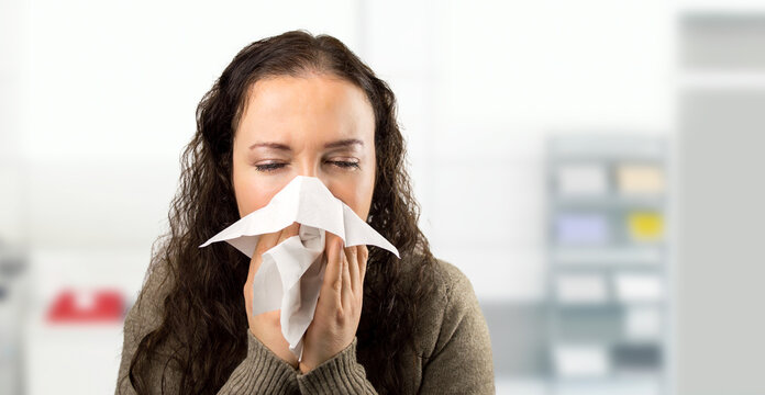 Office, blowing nose or sick woman with tissue, flu or allergy with cold, business or illness at desk. Infection, secretary or female receptionist sneezing with toilet paper, virus or fever disease
