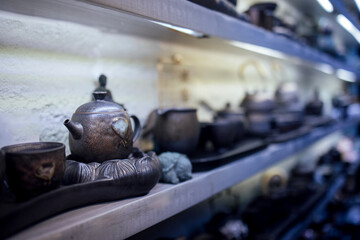 Fototapeta premium Traditional ceramic teapots and cups displayed on a wooden shelf in a tea shop, showcasing various shapes and sizes with a soft, illuminated background