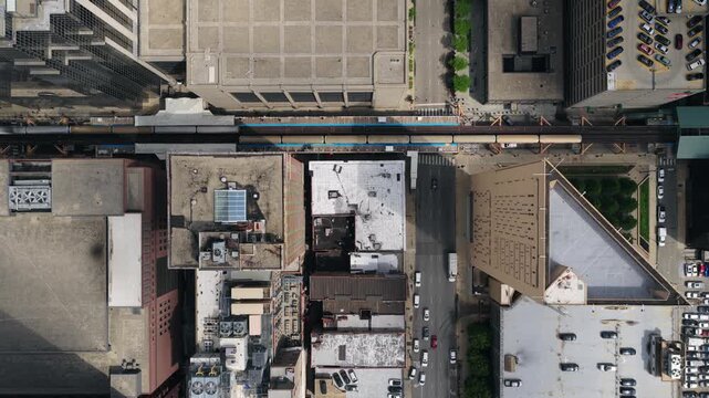 Top down showing Chicago's Loop elevated train traveling between skyscrapers with city traffic moving on streets below and parking lots
