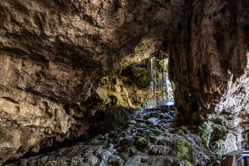 Underground waterfall cascade inside limestone cave tunnel with green moss rock. Kaklik cavern interior with water stream, geological landmark under day light, Denizli, Anatolia, Turkey. © Vlad Rakin