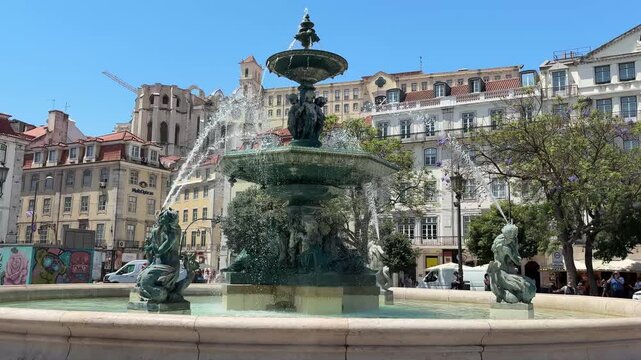 Historic fountain at Rossio Square with blooming jacaranda and Carmo Convent in Lisbon