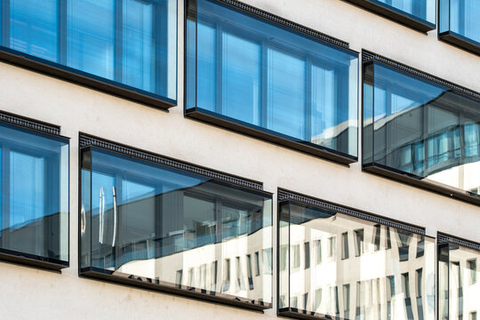 Repeated urban architecture windows stretch across a glass facade, where railing lines, building reflection and exterior structure create layered geometric rhythm