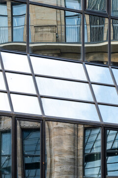 Vertical urban architecture view studies a glass facade against brick building windows, with diagonal grid pattern, reflection, exterior detail and layered structure