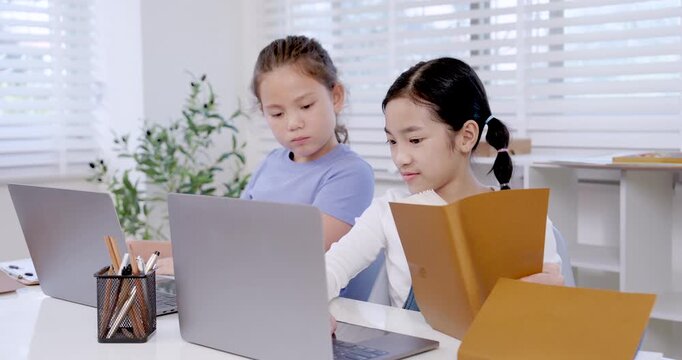 Asian preteen girl holding folder while caucasian girl typing on laptop in classroom representing teamwork collaboration education project digital learning childhood study communication productivity