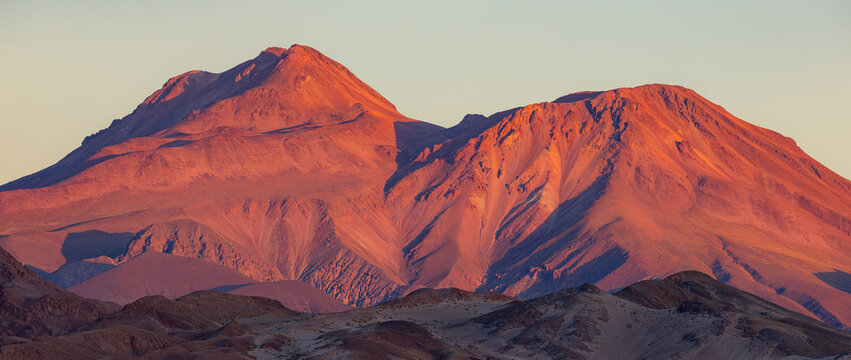 View of the reddish mountain peaks glowing under the warm light of the golden hour in the arid desert landscape of Toconao, Antofagasta, Chile.