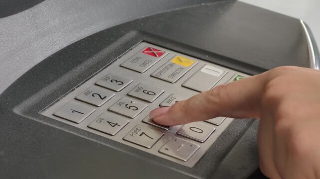 Close-up of a female hand entering a secure PIN code on a metallic ATM keypad during a transaction. The shallow depth of field focuses on banking security and financial technology.