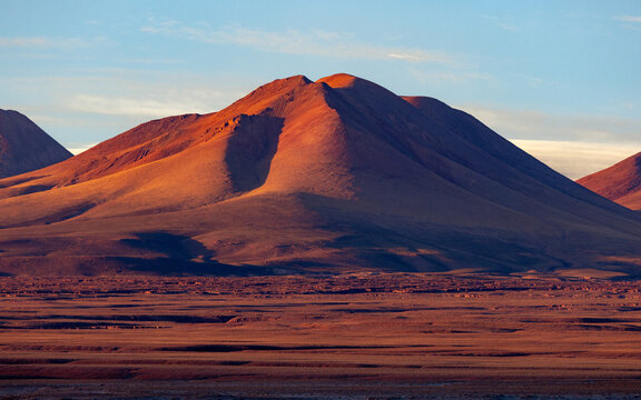 View of red volcanic mountains glowing in the sunset light across the arid Atacama Desert landscape Toconao, Antofagasta, Chile.