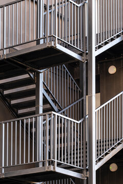 Metal stairs and railing form a dense exterior structure in urban architecture, where shadow, facade, landing and vertical lines shape the access detail