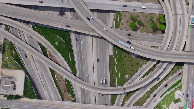 Top down showing car traffic driving on complex interstate highway interchange, with multiple lanes, ramps, overpasses, underpasses creating urban patterns