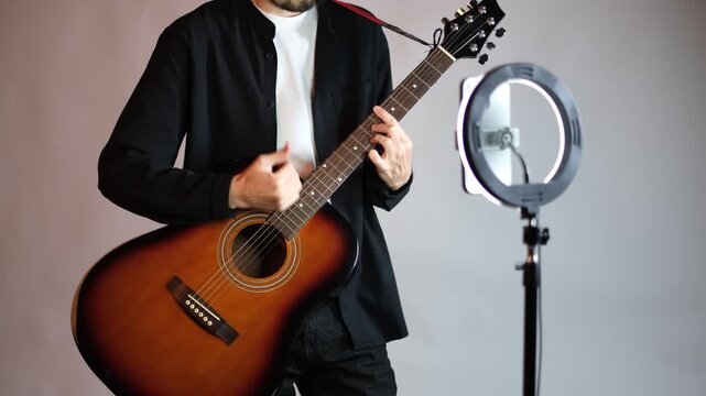 Young musician guitar teacher recording video lesson on phone with ring light in studio

